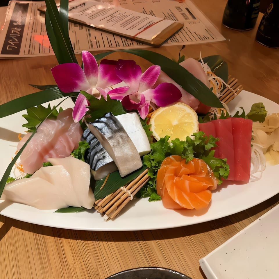 A colorful Sakanaya sashimi platter with various fish, lemon, and purple orchids on a white plate.