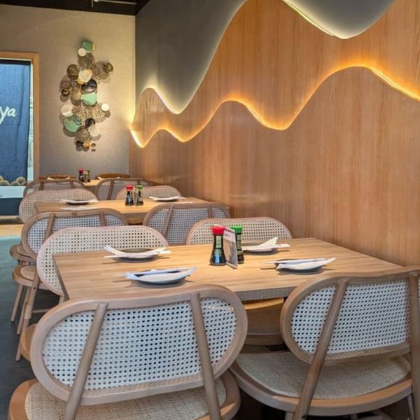 Sakanaya dining room with light wood tables, woven chairs, and a wavy illuminated wall panel.