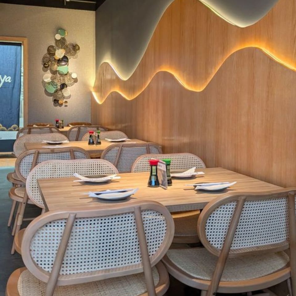 Sakanaya dining room with light wood tables, woven chairs, and a wavy illuminated wall panel.