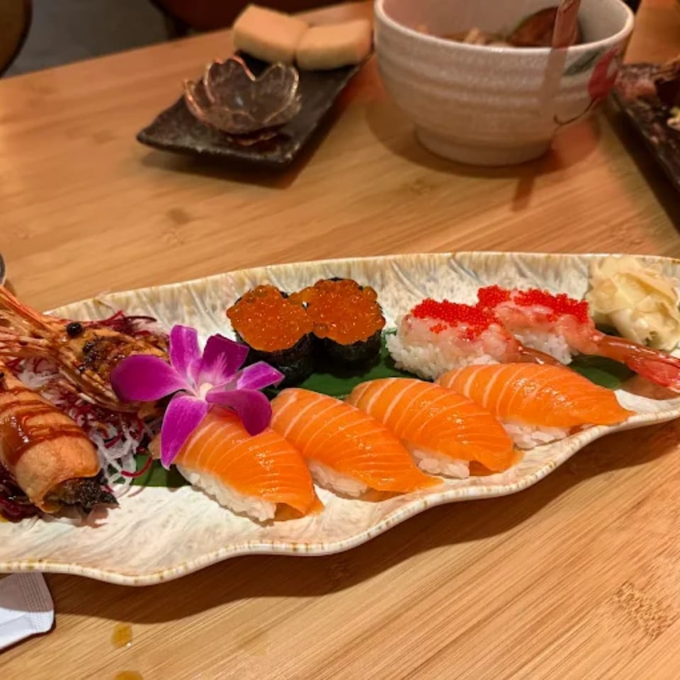 A platter of Sakanaya's fresh salmon nigiri, shrimp nigiri, and gunkan maki with roe, garnished with an orchid.