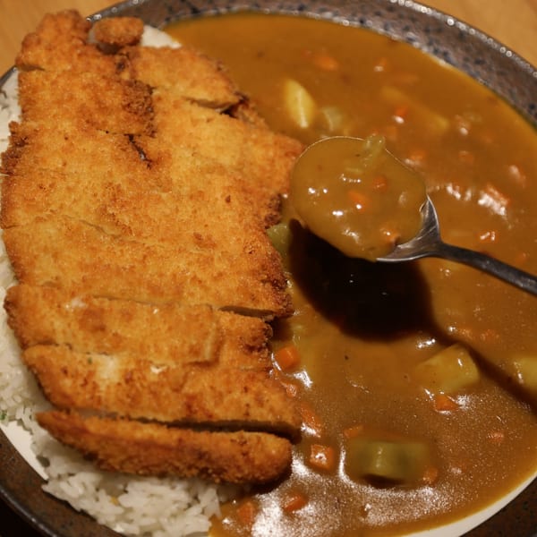 Crispy tonkatsu cutlets and white rice with a side of Japanese curry, a spoon scooping curry.