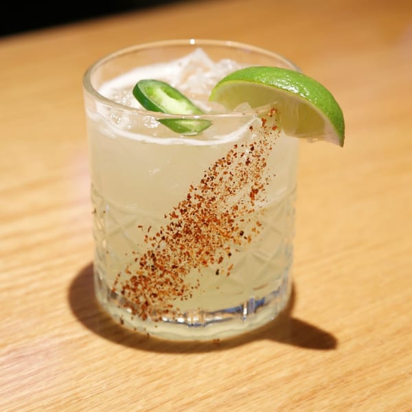 A Sakanaya Japanese restaurant cocktail with lime, jalapeño, and chili powder on a wooden table.