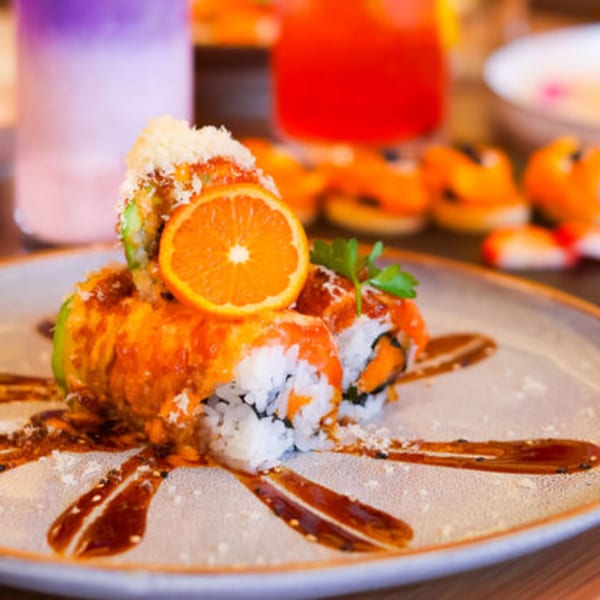Sakanaya sushi roll with orange slice, sauce, and grated cheese on a plate.