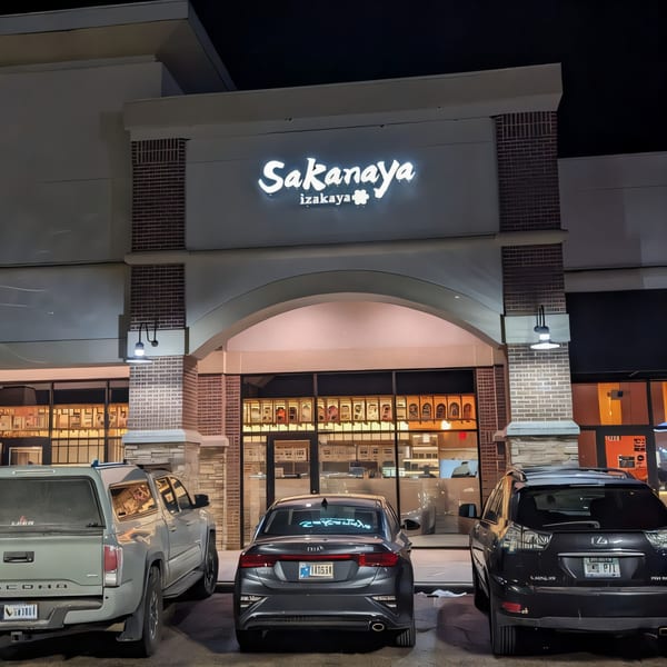 Exterior night view of Sakanaya Japanese restaurant with its glowing sign and parked cars.