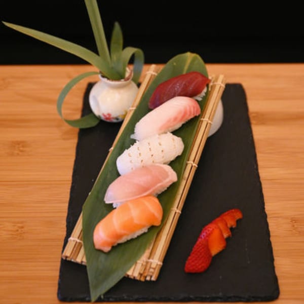 Assorted Sakanaya nigiri sushi, including tuna, salmon, and white fish, on a bamboo mat with a strawberry.