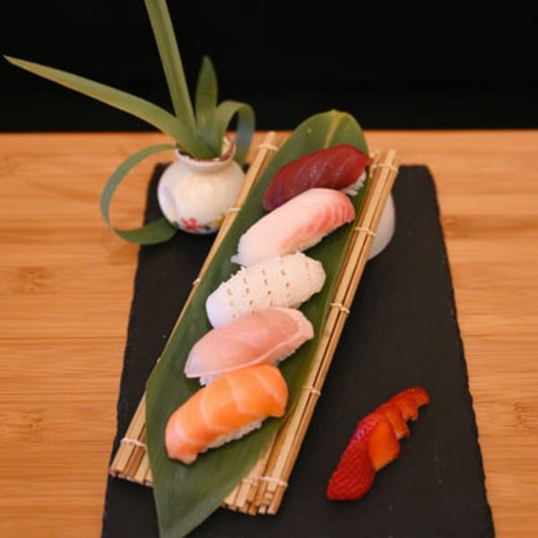 Five pieces of Sakanaya sushi, including salmon and tuna, arranged on a bamboo mat.