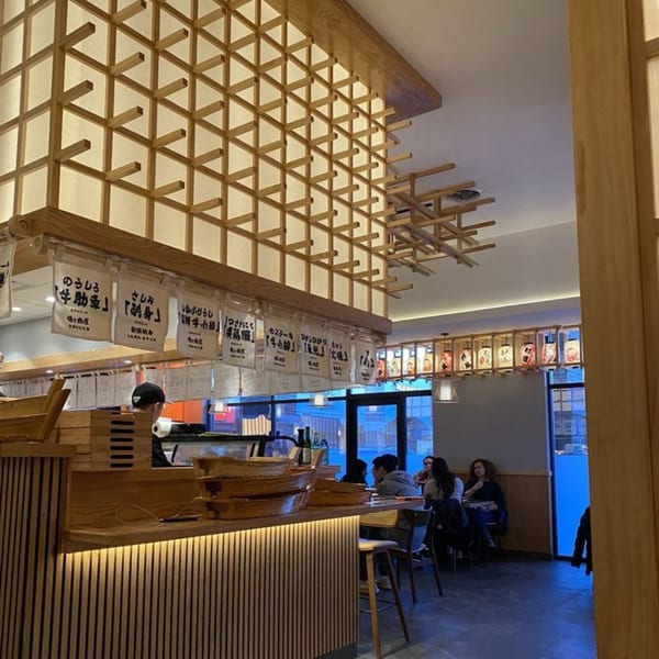 Interior of Sakanaya, a Japanese restaurant, with wooden lattice decor, a sushi bar, and diners.